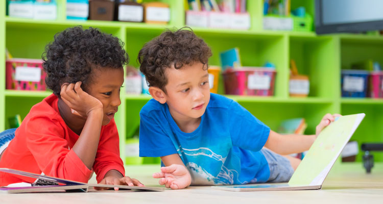 Two young boys on floor, reading book in preschool library