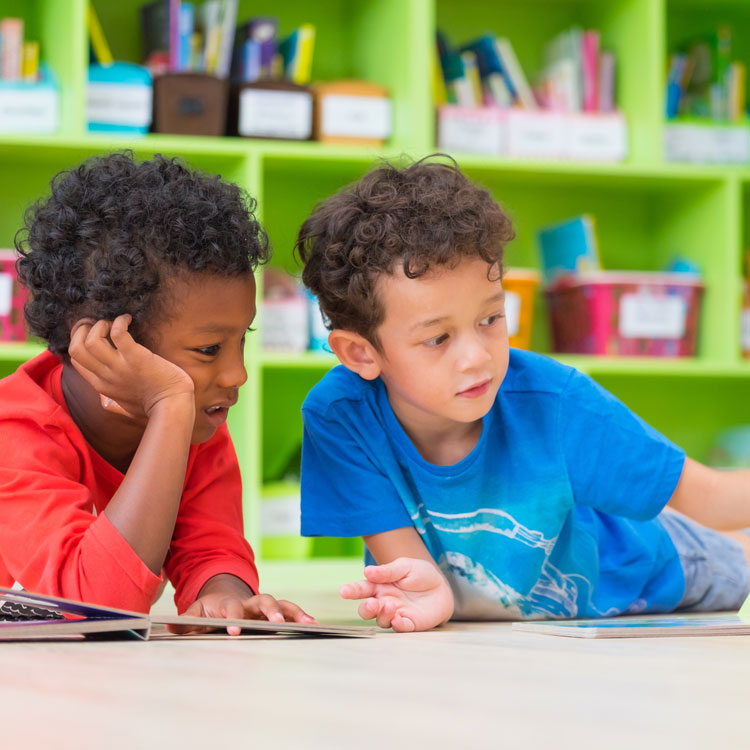 Two young boys on floor, reading book in preschool library